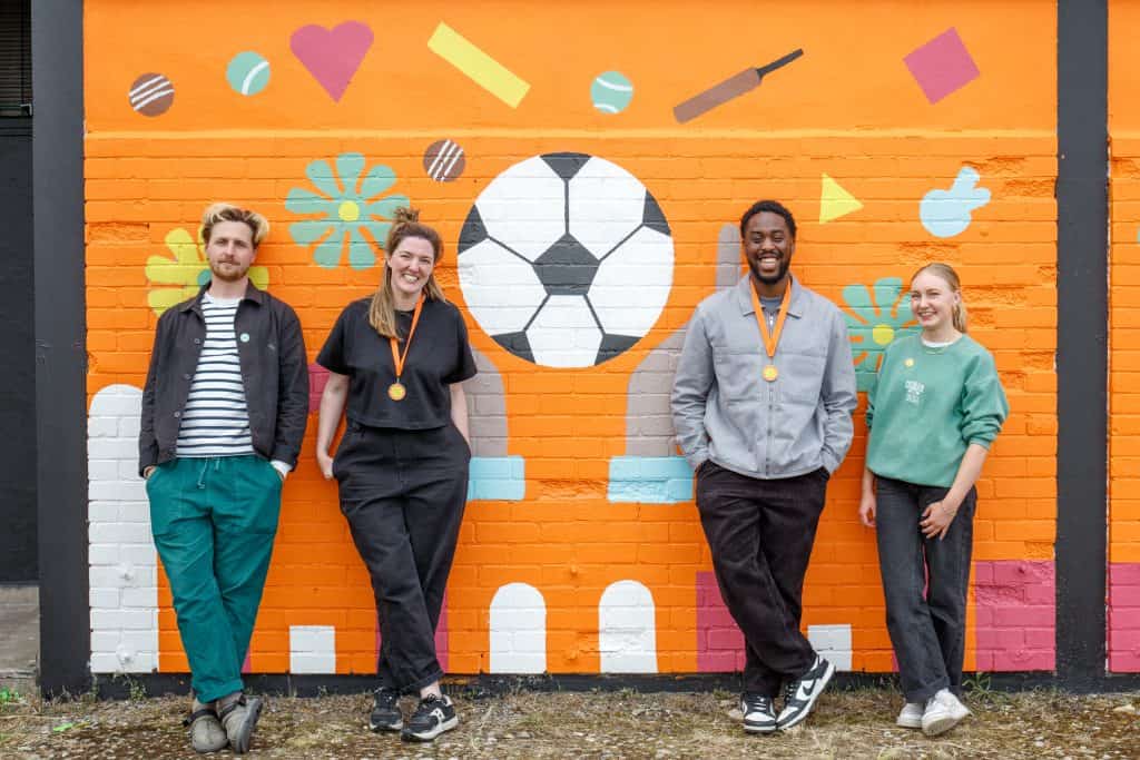 The design team standing in front of a mural featuring a football 