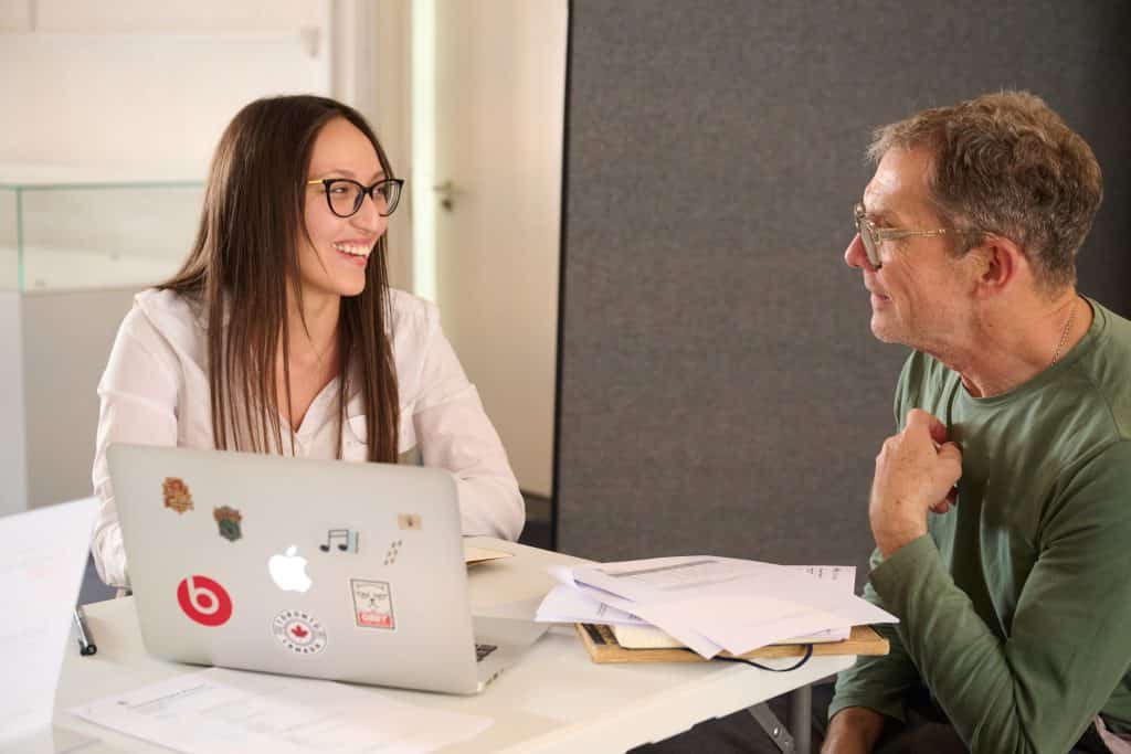 Young woman smiles at man with laptop open.